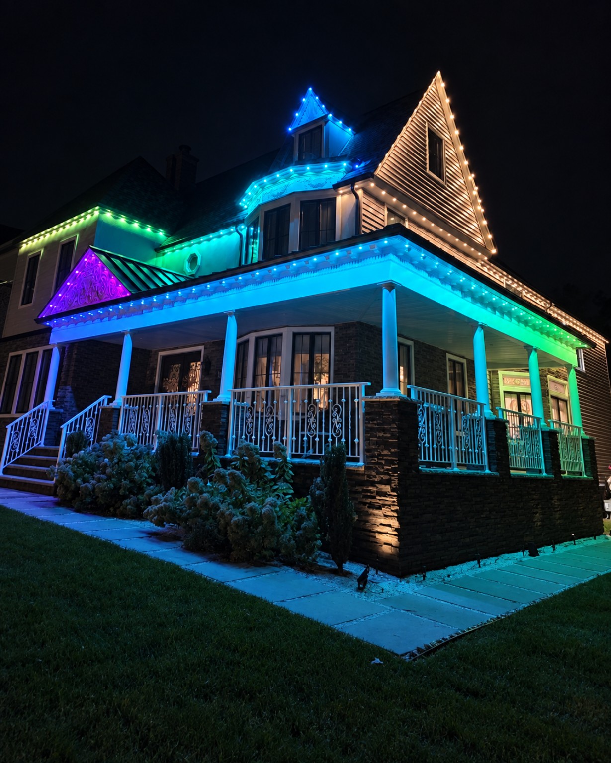 Completed Rutherford home with blue, green, purple and warm white lighting along the rooflines and wraparound porch